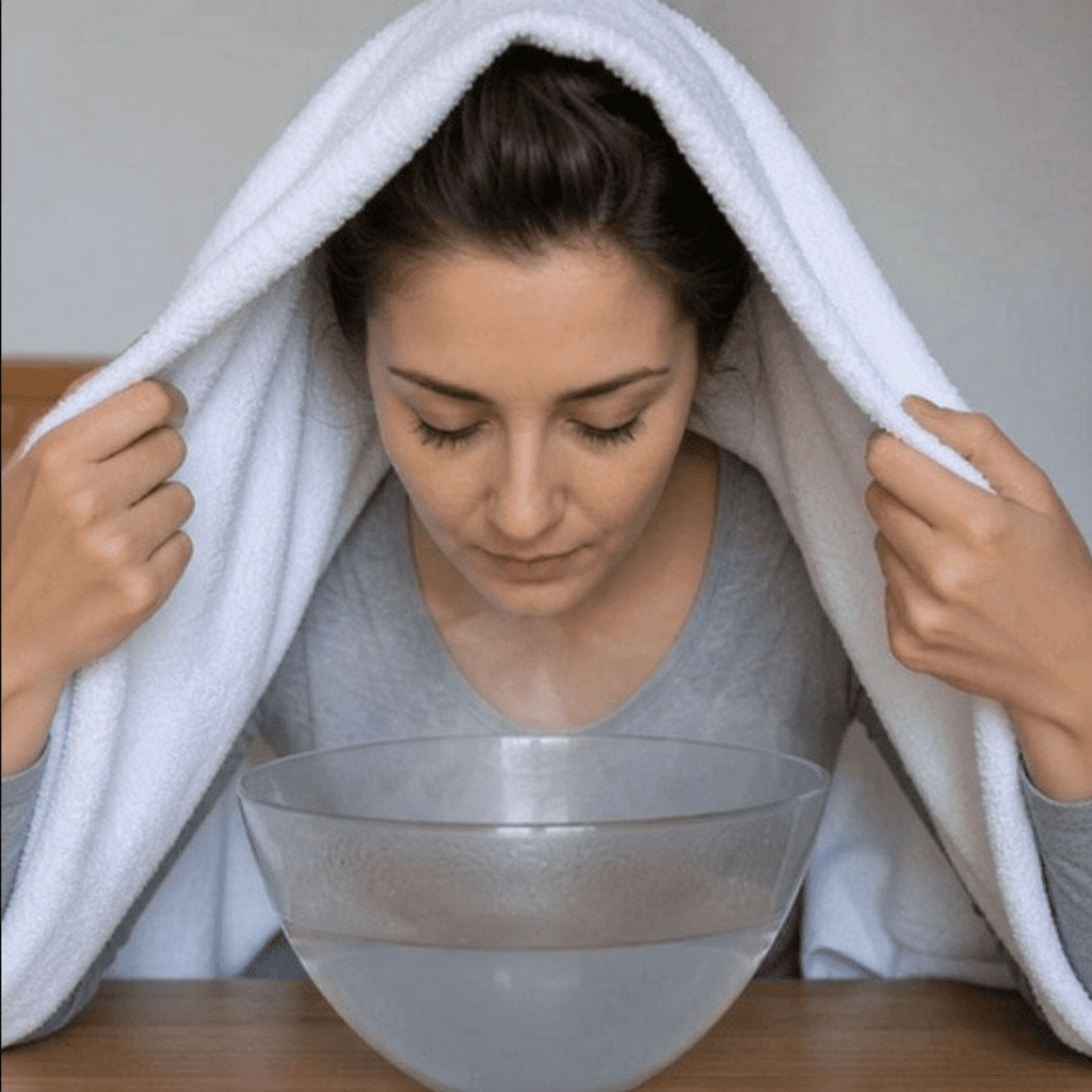 Eine Frau inhaliert heißen Wasserdampf mit einem Handtuch über dem Kopf